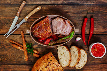 Wall Mural - Baked sliced pork loin in ceramic form with fork, knife and homemade rustic bread on dark rustic background. Roasted pork served with grilled vegetables and tomato sauce. Cozy village dinner...