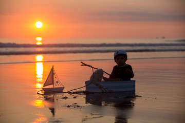 Canvas Print - Cute baby child, sweet boy, playing with boat, teddy bear and fishes on sunset at the edge of the ocean