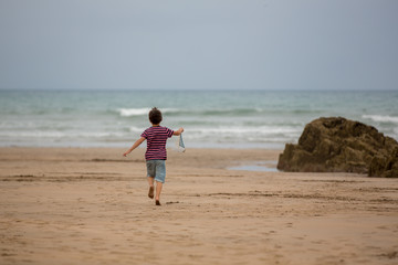 Canvas Print - Child plays with sand on beach. Cute preschool boy with toy ship on beach. Stormy seaside sgore and kid playing