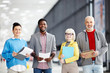 © pressmaster - Group of smiling multiracial coworkers standing in office hall with papers and looking at camera