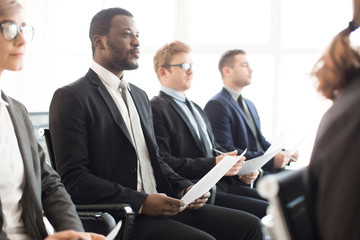 Group of multiethnic coworkers with papers sitting in hall and listening to presentation on business meeting