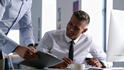 Canvas Print - Handsome smiling office worker using computer and talking about documents with his colleague in office