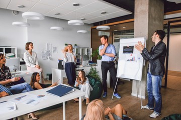 Wall Mural - Corporate meeting of creative entrepreneurs in the office, a man standing behind a magnetic Board with funding schedules