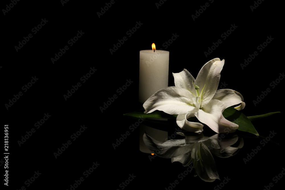 Beautiful lily and burning candle on dark background with space for text. Funeral flower - obrazy, fototapety, plakaty 