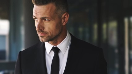 Wall Mural - serious business man dressed in suit using smartphone while walks outside a glass building