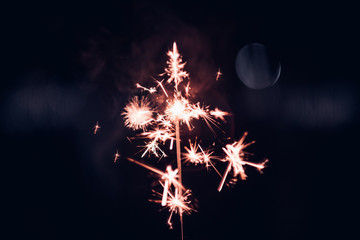 Poster - Hand holding burning Sparkler blast on a black background at night,holiday celebration event party,dark vintage tone