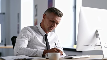 Canvas Print - Handsome smiling office worker using computer and talking on smartphone while working in office