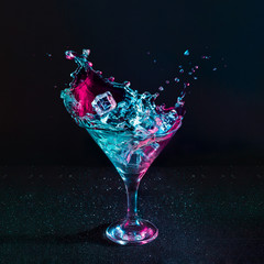 Wall Mural - Martini cocktail drink splash with ice cubes in neon iridescent pink and blue colors. Minimal night party life concept.