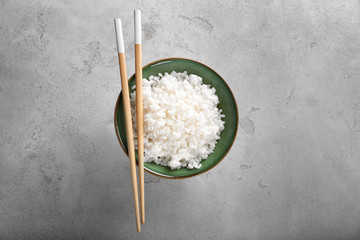 Bowl with boiled white rice and chopsticks on grey textured background