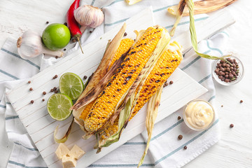 Board with tasty grilled corn cobs and sauce on white table