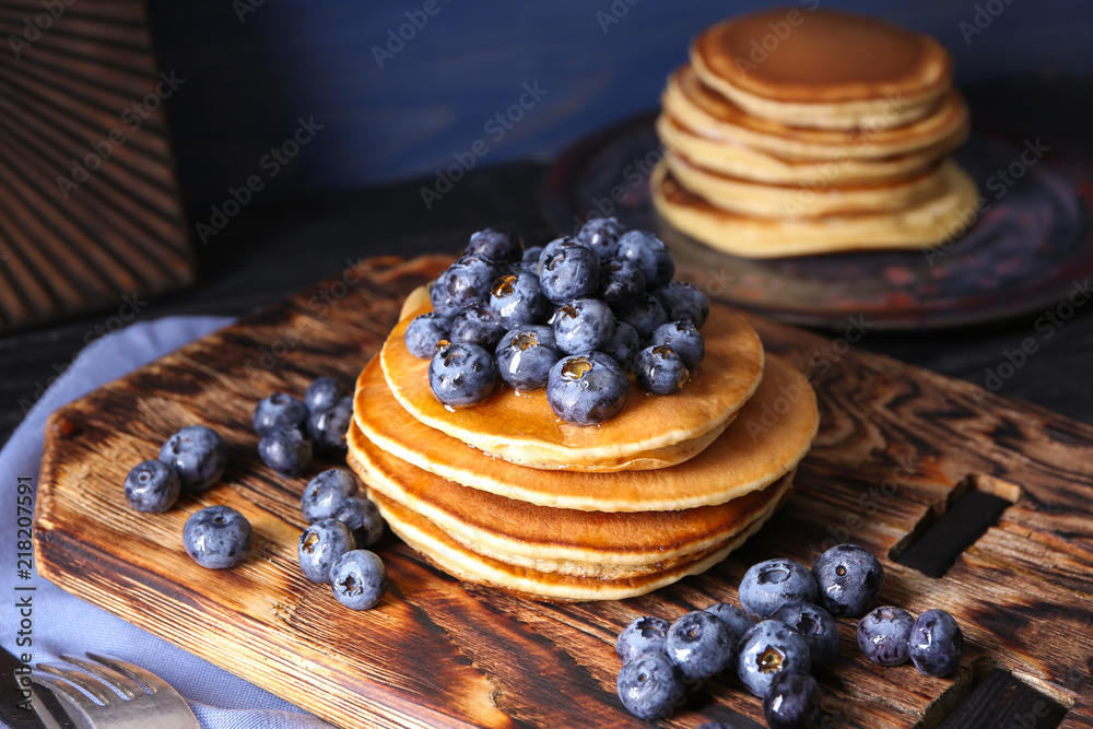 Board with tasty pancakes and blueberries on table