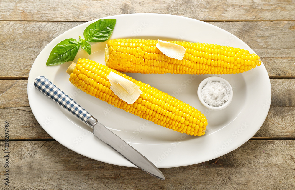 Plate with tasty corn cobs, butter and salt on wooden table