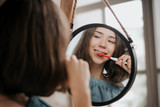 Fototapeta Do akwarium - Beautiful young woman brushing teeth in front of her bathroom mirror.