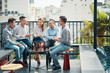 © DragonImages - Cheerful Asian friends sitting on terrace with beer bottles on table and relaxing in sunlight on urban background