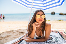 Pretty Woman In Sunglasses In Swimsuit Lying On Sandy Beach With Colorful Beach Umbrella Near Sea