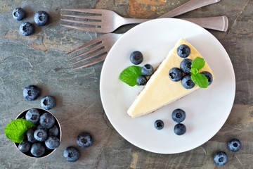 Poster - Slice of cheesecake with blueberries on a plate. Top view scene over a dark background.