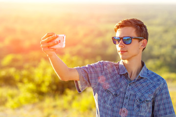 cute guy takes a selfie on the phone in the sun