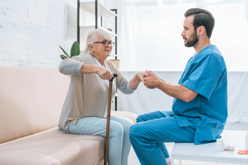 Wall Mural - side view of male nurse helping senior woman with walking stick