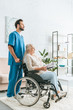© LIGHTFIELD STUDIOS - side view of social worker pushing wheelchair with senior woman holding newspaper and eyeglasses