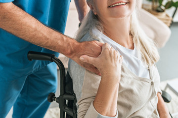 Wall Mural - cropped shot of smiling senior woman in wheelchair holding hand of caregiver