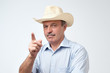 © Viktor Koldunov - Serious mature hispanic man in cowboy hat showing index fingers up, giving advice or recommendation