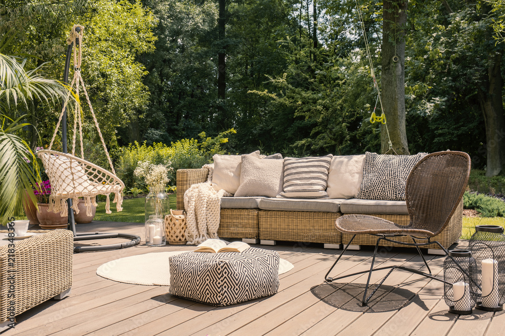 Pouf and rattan chair on wooden patio with settee in the garden during summer. Real photo - obrazy, fototapety, plakaty 