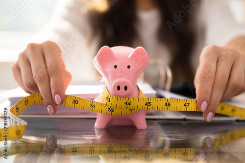 Fotografie, Obraz Businesswoman Measuring Piggybank With Measuring Tape
