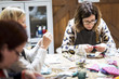 © Mint Images - Group of women sitting around a table in a workshop, making fabric flowers.