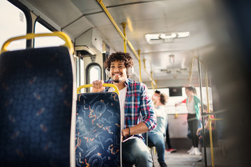 Young beautiful Afro-American man is sitting alone in a bus full of people.