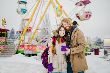 Young couple in love with a happy young man with a beard and a woman on a background of a fucking colossus, a Ferris wheel resting, a date in an amusement park in the winter in the Christmas holidays.