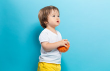 Toddler Boy Holding A Pumpkin For Halloween On A Blue Background