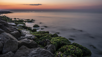 The infinity horizon above the sea. The stone beach with moss and eyelashes. The waves flow to the coastline. Morning atmosphere before sunrise.