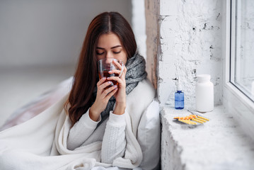 Sickness and illness. Sick unhealthy woman drinking warming drink indoors. Cold and flu. Closeup of beautiful young girl with hot cup of tea in hands.