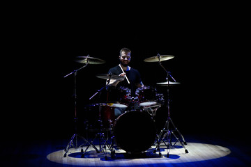 Drummer in a cap and headphones plays drums at a concert under white light in a smoke