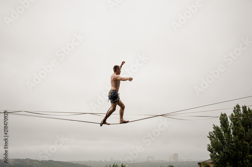 Fotografía Strong and brave man walking on a slackline against the grey sky