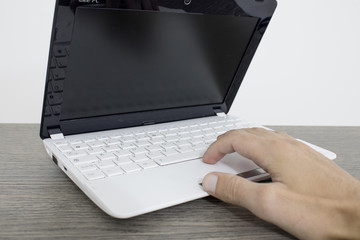 A hand is writing with a laptop on a wood table