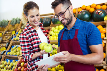 Two young sellers doing inventory with digital tablet in health grocery shop.