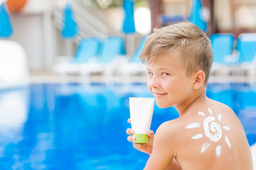 Poster - Boy with sun painted by sun cream on shoulder is showing a tube. Summer vacation concept. Space for text