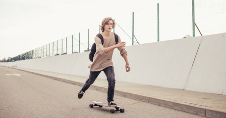 Wall Mural - young boy riding longboard on boardwalk, warm summer time