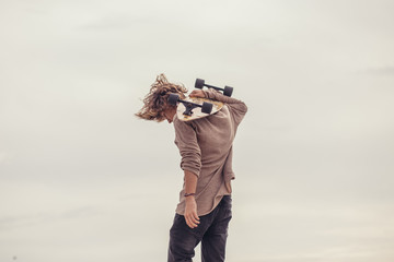 Wall Mural - stylish young blond curly hair man holding skateboard on shoulders and smile