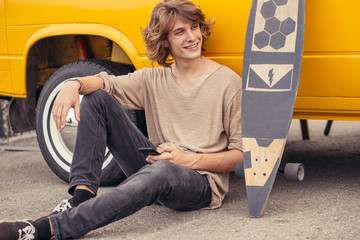 Wall Mural - Young hipster man sitting on longboard using his phone