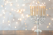 Hanukkah Menorah With Candles On Table Against Blurred Lights
