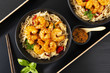 Fried prawns and rice noodles with spices on a black plate. Black background. Eastern food. Copy space. Horizontal shot.