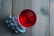 glass of red wine and grapes on black wood table background