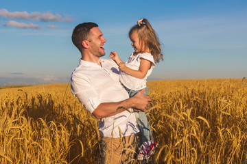 Happy family - father holding daughter in his arms in the middle of a wheat field against a blue summer sky