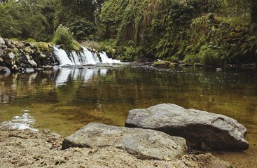 Scenic landscape of the river Neiva in the middle of the forest in Portugal. Waterfall in the background and two large stones in the foreground. Clear, clean water with a sense of tranquility