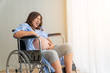 © Birdland - Portrait A pregnant woman sitting on a wheelchair near the balcony. She has very abdominal pain. She needs help And want to see a doctor. Copy space.