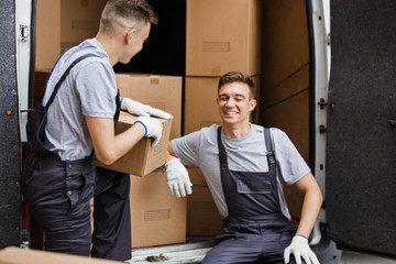 Wall Mural - Two young handsome movers wearing uniforms are laughing while un