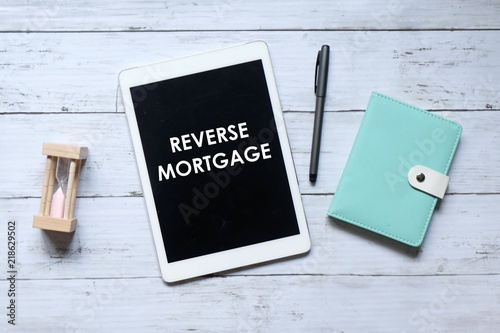 Fotografía Top view of hourglass,notebook,pen and tablet pc written with REVERSE MORTGAGE on wooden background