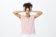 © Cookie Studio - Cannot hold emotions inside. Portrait of stressed dark-skinned emotive woman in striped t-shirt, holding hands on head, closing eyes and shouting out loud, being in depression and angry over gray wall